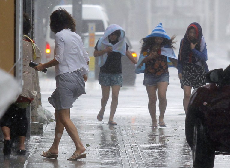Women walk amid strong winds on a street in Naha, Okinawa, southern Japan, Tuesday, July 8, 2014. Powerful Typhoon Neoguri pounded across the southern Japanese islands of Okinawa on Tuesday, as residents took refuge from destructive winds, towering waves and storm surges. Airports closed and residents were evacuated from low-lying areas and shorelines as the typhoon passed over Okinawa, packing sustained winds of 175 kilometers (108 miles) per hour and gusts up to 250 kph (154 mph), the Japan Meteorological Agency said. (AP Photo/Kyodo News) JAPAN OUT, CREDIT MANDATORY