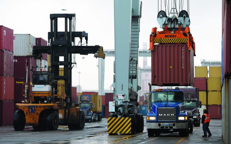 FILE - In this Dec. 18, 2012 file photo, a truck driver watches as a freight container, right, is lowered onto a tractor trailer by a container crane at the Port of Boston in Boston. The crane and a reach stacker, left, are operated by longshoremen at the port. The longshoremen's union may strike if they are unable to reach an agreement on their contract, which expires Dec. 29, 2012. A walkout by dock workers represented by the International Longshoremen's Association would bring commerce to a near halt at ports from Boston to Houston. (AP Photo/Steven Senne, File)