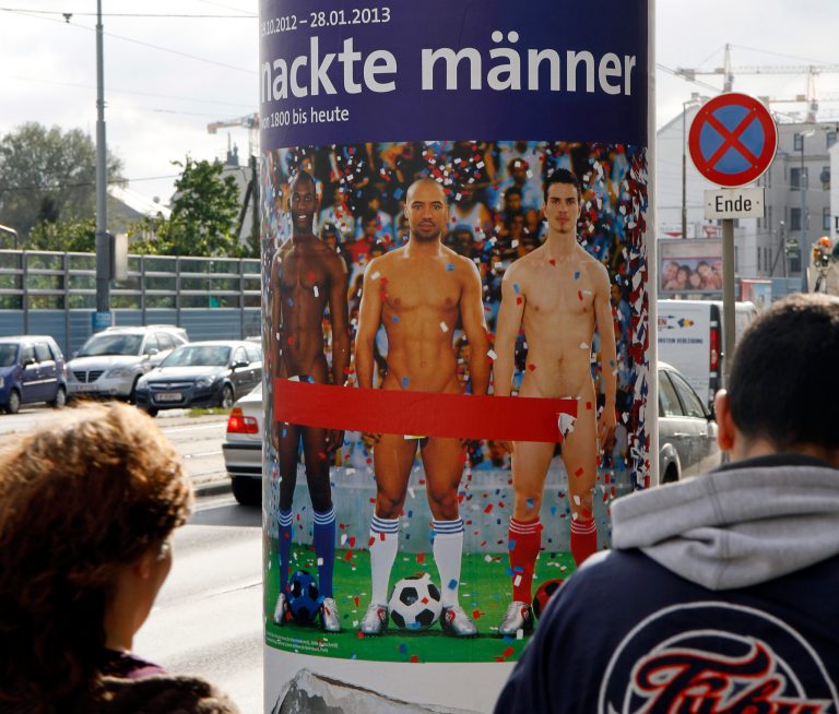   FILE - In this Oct. 18, 2012 file photo two people walk past a poster showing three naked men which has had red tape added to cover the sensitive parts of the three men, in Vienna, Austria. Poster reads: 