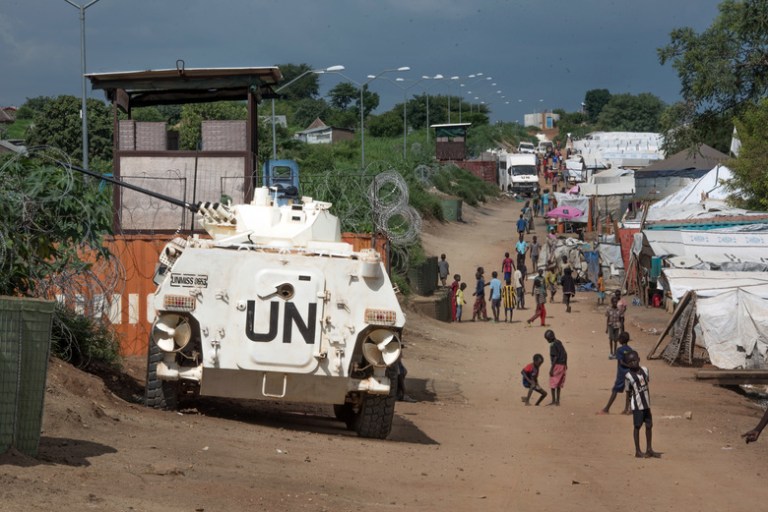 FILE - In this Monday, July 25, 2016 file photo, some of the more than 30,000 civilians sheltering in a United Nations base in South Sudan's capital Juba for fear of targeted killings by government forces walk by an armored vehicle and a watchtower manned by Chinese UN peacekeepers. When South Sudan's president signed a peace deal a year ago to end the country's civil war he added 16 reservations to the agreement, which have now become a map of how it has unraveled. (AP Photo/Jason Patinkin, File)