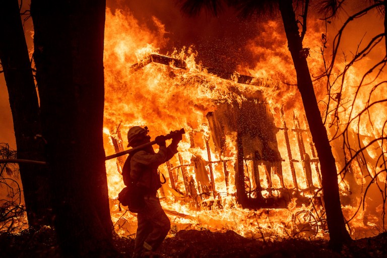 Firefighter Jose Corona sprays water as flames consume from the Camp Fire consume a home in Magalia, Calif., on Friday, Nov. 9, 2018.  
