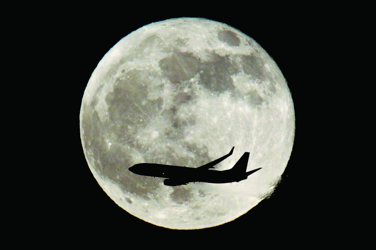 FILE - In this Saturday, Dec. 10, 2011, file photo, a plane flies over New Jersey with the full moon in the background, in Newark, N.J. The merger of US Airways and American Airlines has given birth to a mega airline with more passengers than any other in the world. (AP Photo/Julio Cortez, File)