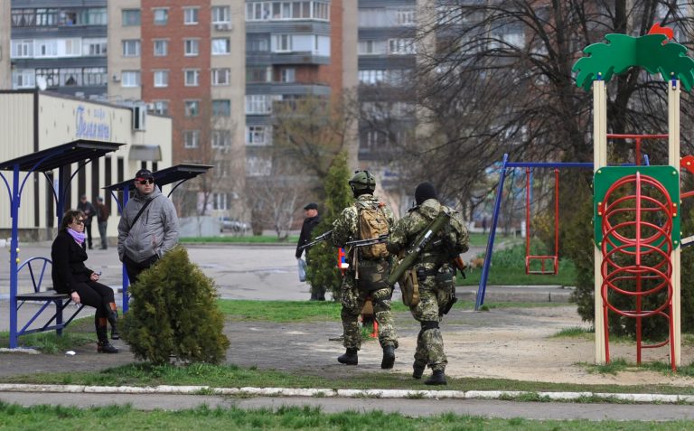 Armed pro-Russian activists walk through a children's playground near to the seized Ukrainian regional administration building in the eastern Ukrainian town of Slovyansk,  Ukraine, Monday, April 14, 2014.  Ukraine's acting president urged the United Nations on Monday to send peacekeeping troops to eastern Ukraine, where pro-Russian gunmen kept up their rampage of storming and occupying local government offices, police stations and a small airport. (AP Photo/Evgeniy Maloletka)