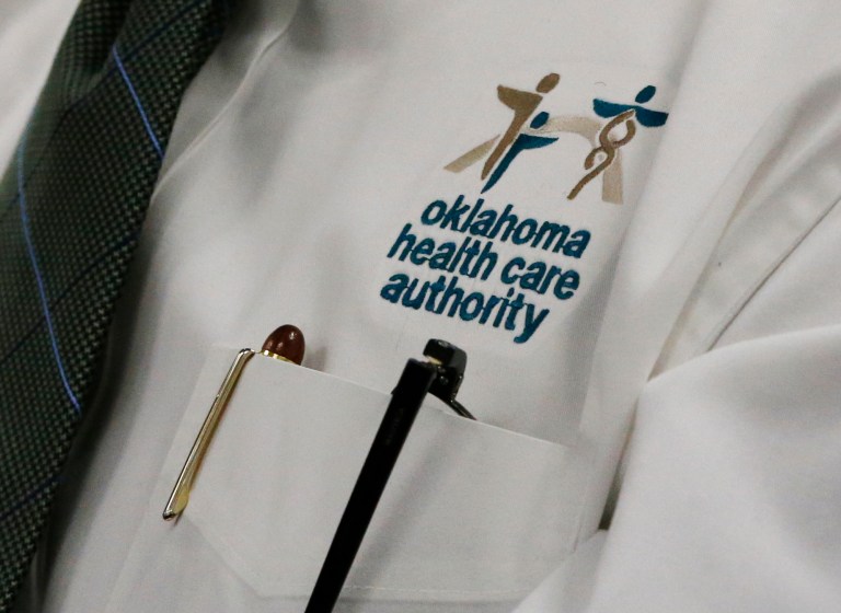 An audience member wears an Oklahoma Health Care Authority shirt during an OHCA board meeting in Oklahoma City, Tuesday, July 1, 2014. Pediatricians and wheelchair providers from across the state warned that cuts to reimbursement rates could force them to stop providing services to some of Oklahomaâs neediest citizens. The Oklahoma Health Care Authority Board unanimously approved a 7.75 percent provider rate cut during a special meeting as it grapples with a $104 million hole in its budget for the new fiscal year. (AP Photo/Sue Ogrocki)
