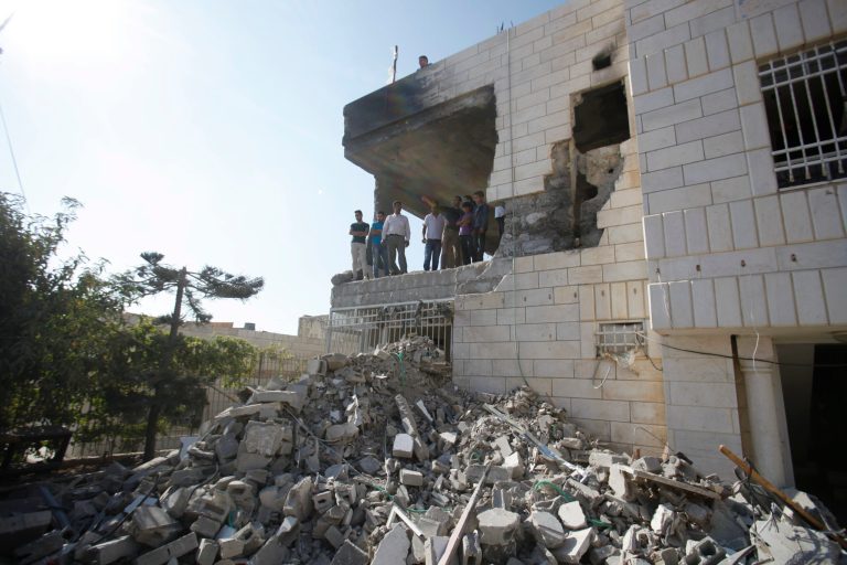 Palestinians stand in what is left of the home of Amer Abu Aisheh, one of three Palestinians identified by Israel as suspects in the killing of three Israeli teenagers, after it was demolished by the Israeli army in the West Bank city of Hebron, Monday, Aug. 18 , 2014. (AP Photo/Nasser Shiyoukhi)