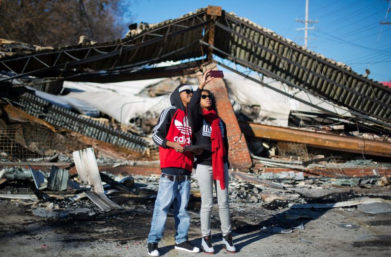Darius Crenshaw, left, and his sister Keona, both of Ferguson, Mo., take a selfie while standing in front of a burned down beauty salon from last night's riots, Tuesday, Nov. 25, 2014, in Ferguson, Mo. (AP Photo/David Goldman)
