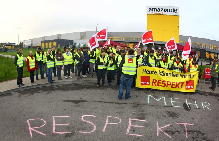 Employees of Amazon gather in front of an Amazon building during a strike in Graben, southern Germany, Monday, Sept. 22, 2014. Workers at four of Amazon.com's German distribution centers have started a two-day strike in a long-running dispute over wages. The ver.di union said workers at the American online retailer's logistics centers in Leipzig, Bad Hersfeld, Graben and Rheinberg will stay off the job until Tuesday evening. Banner reads: 