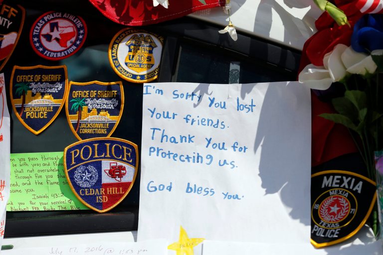 A note left behind attached to a police cruiser at a makeshift memorial in front of the headquarters of the Dallas Police Department sits surrounded by law enforcement badges, Tuesday, July 19, 2016, in Dallas. The memorial pays tribute to the five fallen police officers who were killed by a gunman during a protest earlier this month in Dallas. (AP Photo/Tony Gutierrez)