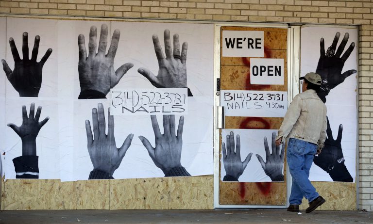 A man who declined to be identified stands outside a boarded up business Thursday, Nov. 20, 2014, in Ferguson, Mo. Ferguson and the St. Louis region are on edge in anticipation of the announcement by a grand jury whether to criminally charge Officer Darren Wilson in the killing of 18-year-old Michael Brown. (AP Photo/Jeff Roberson)