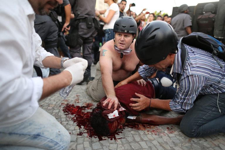Local TV cameraman Andrade Santiago is helped after he was injured during violent clashes with police during a protest against a bus fare increase in Rio de Janeiro, Thursday, Feb. 6, 2014. Police said Thursday that the cameraman for the Band TV station was injured in the protest and is in serious condition. It was not clear if the journalist was hit by a homemade explosive thrown by protesters or a stun grenade shot by police. (AP Photo/Leo Correa)