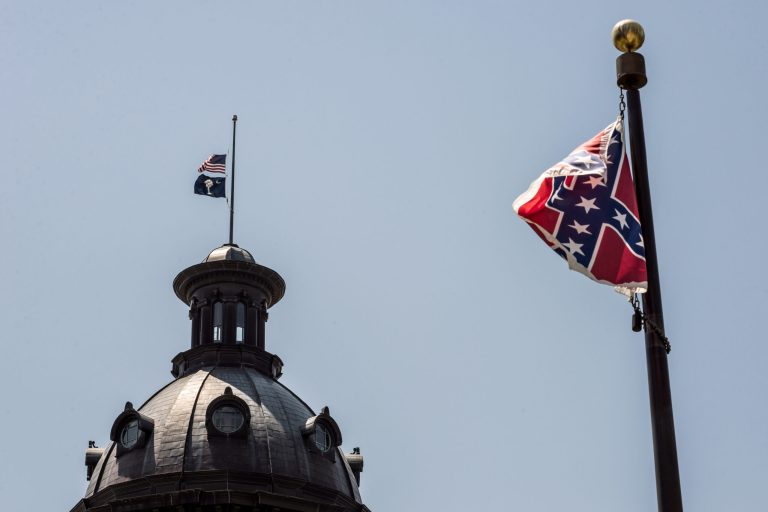 The South Carolina and American flags fly at half mast as the Confederate flag unfurls below at the Confederate Monument June 18, 2015 in Columbia, South Carolina. Legislators gathered Thursday morning to honor their co-worker Clementa Pinckney and the eight others killed yesterday at Emanuel AME Church in Charleston, S.C. (Photo by Sean Rayford/Getty Images)
