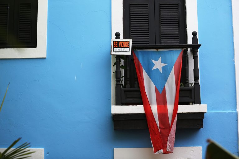 A for sale sign is seen hanging from a balcony next to a Puerto Rican flag in Old San Juan as the island's residents deal with the government's $72 billion debt on July 1, 2015 in San Juan, Puerto Rico. (Photo by Joe Raedle/Getty Images)