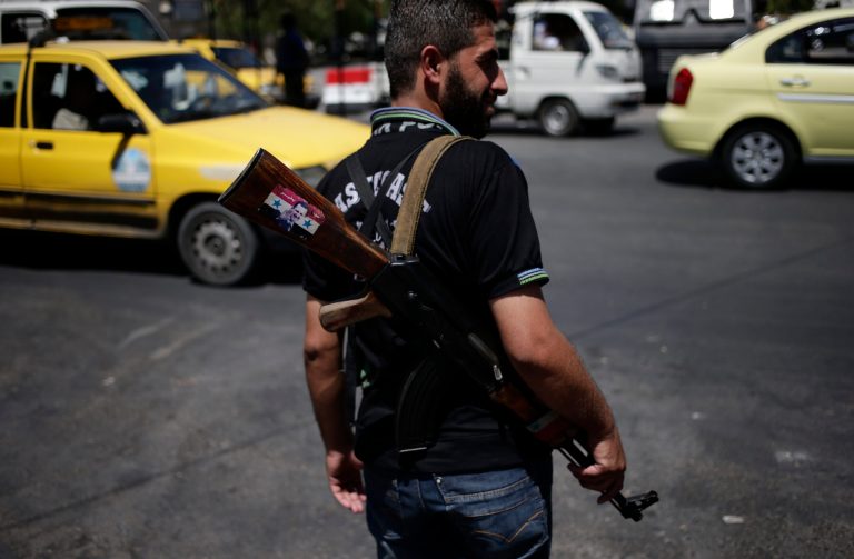 A Syrian military soldier holds his AK-47 with a sticker of Syrian President Bashar Assad and Arabic that reads, 