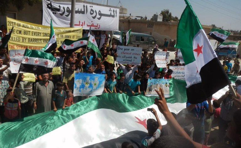 In this photo provided by an anti-Bashar Assad activist group Edlib News Network (ENN), which has been authenticated based on its contents and other AP reporting, anti-Syrian government protesters carry banners and a giant Syrian revolution flag during a demonstration in Idlib province, northern Syria, Friday, Aug 22, 2014. The death toll from three years of Syria's civil war has risen to more than 191,000 people, the United Nations reported Friday. (AP Photo/Edlib News Network ENN)