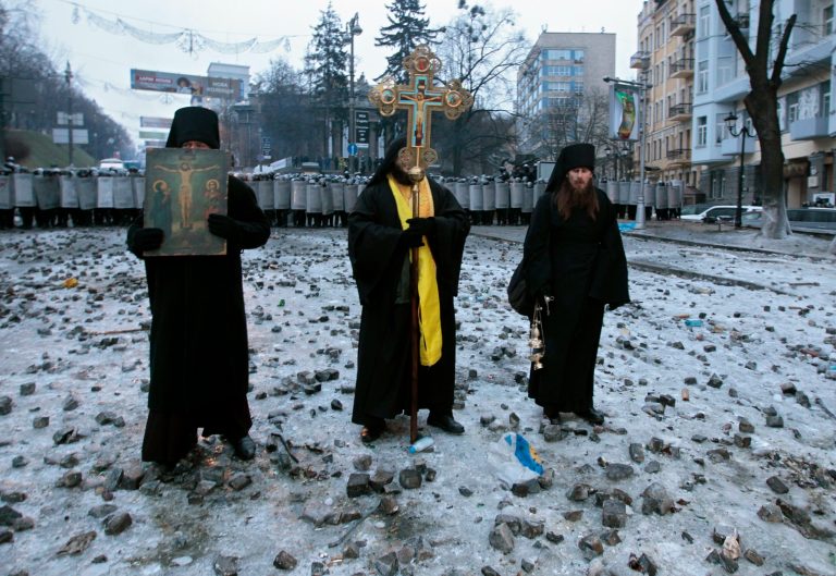 Orthodox priests pray as they stand between pro-European Union activists and police lines in central Kiev, Ukraine, Tuesday, Jan. 21, 2014. Anti-government protesters have held their ground through a night of violent street clashes in the Ukrainian capital, despite police moving in to dismantle barricades erected in a street leading to government offices. Police attempted to move in on the protest camp early Tuesday, but faced fierce resistance from demonstrators who tossed fire bombs and stones in their direction. (AP Photo/Sergei Chuzavkov)