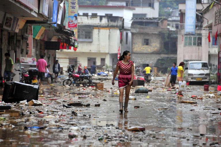 In this photo released by China's Xinhua News Agency taken on Saturday, May 24, 2014, residents walk on a street after flooding subsided in Shitan Town of Qingyuan, south China's Guangdong Province. The Chinese state news agency is reporting 12 people have died in widespread flooding in southern China.  Xinhua News Agency said the flooding affected 649,000 people in Qingyuan city in Guangdong province as of Saturday afternoon, with 3,300 houses collapsing. (AP Photo/Xinhua, Tian Jianchuan) NO SALES