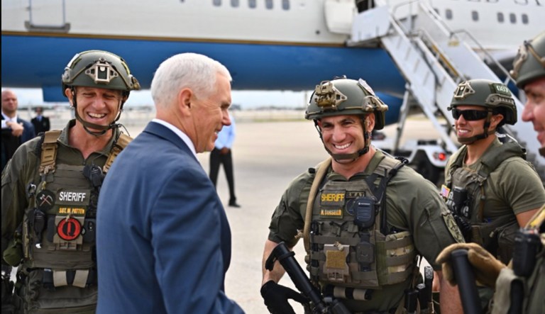 In this screenshot from a deleted tweet, Vice President Mike Pence is pictured next to a person with a patch referencing QAnon (left).