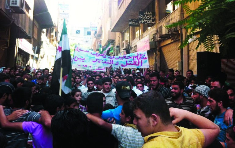 In this citizen journalism image provided by Shaam News Network SNN, taken on Friday, July 13, 2012, Syrians chant slogans during a demonstration in Damascus, Syria. On Sunday Syria denied U.N. claims that government forces used heavy weapons during a military operation that left scores dead. Partial translation of Arabic on the banner reads, 