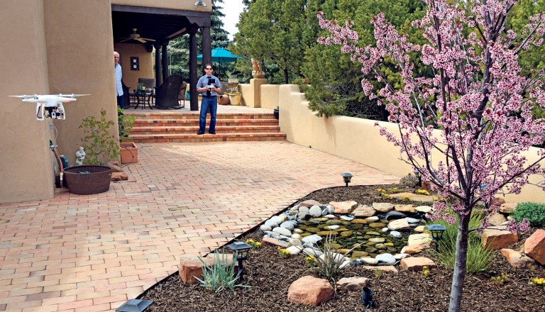 Santa Fe, New Mexico homeowner Hal Wingo, left, watches as Brian Tercero, of Keller Williams Realty flies his  DJI Phantom drone as he takes video of the garden on April 18, 2014, in Santa Fe, N.M.  (AP Photo/The Santa Fe New Mexican,  Clyde Mueller)