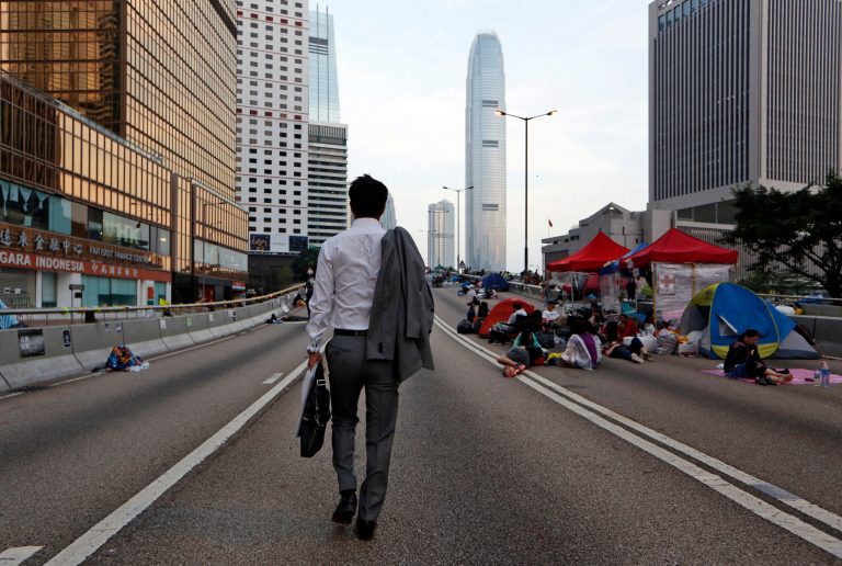 A man walks to work as the pro-democracy student protesters sleep on a roadside in the occupied areas surrounding the government complex in Hong Kong Oct. 6, 2014. Hong Kong's civil servants returned to work and schools were reopening Monday as a massive pro-democracy protest that has occupied much of the city center for the week dwindled. (AP Photo/Kin Cheung)