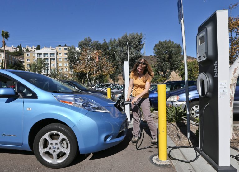 Angie Vorhies plugs in the charging cord to her Nissan Leaf electric vehicle  at a mall Wednesday, Nov. 13, 2013, in San Diego. A New Jersey energy company required by an unusual legal settlement to build an extensive network of electric car chargers throughout California has delivered just 10 percent of what it promised in the first year. (AP Photo/Lenny Ignelzi)