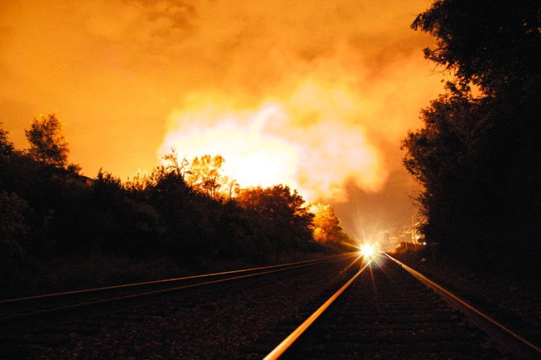 Flames rise from a derailed freight train, left unseen, early Wednesday July 11, 2012 in Columbus Ohio. Part of a freight train derailed and caught fire in Ohio's capital city early Wednesday, shooting flames skyward into the darkness and prompting the evacuation of a mile-wide area as firefighters and hazardous materials crews worked to determine what was burning and contain the blaze.(AP Photo/Chris Mumma)