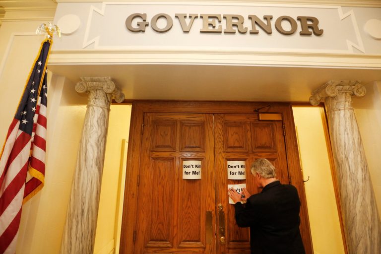Nathaniel Batchelder, with the Oklahoma Coalition Against the Death Penalty, places a sign protesting the death penalty on Gov. Mary Fallin's office at the state Capitol in Oklahoma City Tuesday. (AP Photo/The Oklahoman, Steve Gooch)
