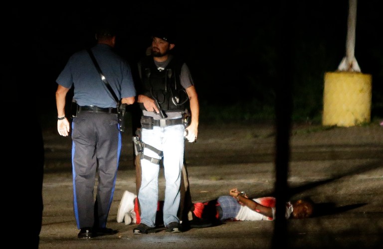 Police stand near a suspect in a parking lot after gunfire during a protest on the anniversary of the death of Michael Brown, Sunday, Aug. 9, 2015, in Ferguson, Mo. (AP Photo/Jeff Roberson)