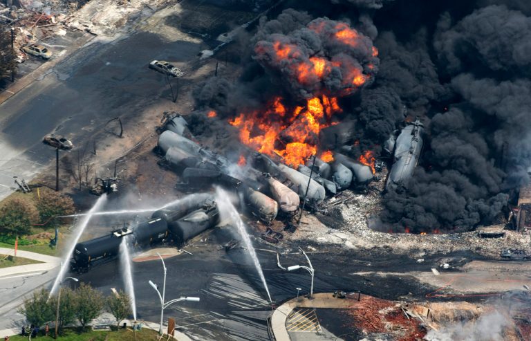 FILE - Smoke rises from railway cars that were carrying crude oil after derailing in downtown Lac Megantic, Quebec, Canada, Saturday, July 6, 2013.  Three employees and the railway company involved in the massive explosion, killing 47 people, will face criminal negligence charges, provincial prosecutors announced late Monday, May 12, 2014. (AP Photo/The Canadian Press, Paul Chiasson, File)