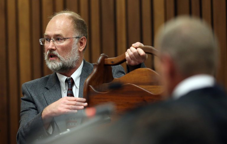 Forensic expert, Roger Dixon, left, holds a court exhibit, a magazine rack, as he answers questions put to him by chief state prosecutor Gerrie Nel , right, during the murder trial of Oscar Pistorius, in Pretoria, South Africa, Thursday, April 17, 2014.  Pistorius is charged with the murder of his girlfriend, Reeva Steenkamp, on Valentines Day in 2013. (AP Photo/Themba Hadebe, Pool)