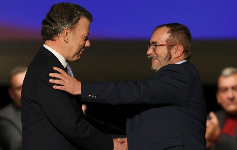 Colombia's President Juan Manuel Santos, left, shakes hands with with Rodrigo Londono, top leader of the Revolutionary Armed Forces of Colombia, FARC, after signing a revised peace pact at Colon Theater in Bogota, Colombia. (AP Photo/Fernando Vergara)
