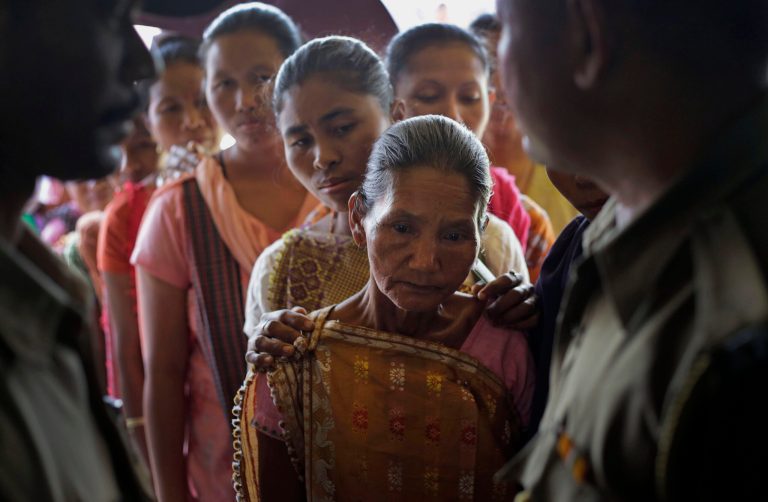 Security officers stand guard at the door as Karbi tribal women in traditional outfits stand in a queue to cast their votes at a polling booth in Diphu, in the northeastern Indian state of Assam, Saturday, April 12, 2014. The multiphase voting across the country runs until May 12, with results for the 543-seat lower house of parliament announced May 16. (AP Photo/Anupam Nath)