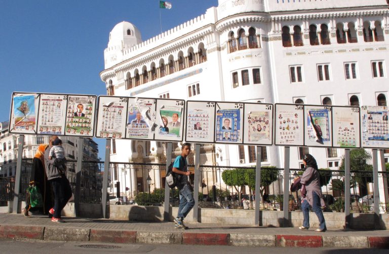   FILE - In this April 30, 2012 file photo, Algerians walk by posters for election lists displayed in front of the main post office in downtown Algiers. Two years after an itinerant Tunisian fruitseller set himself on fire to protest government injustice and ignited uprisings across the Middle East, the three nations of the Maghreb _ Algeria, Tunisia and Morocco_ have taken wildly different paths, from wholesale political change in Tunisia, to business as usual in oil-rich Algeria. (AP Photo/Paul Schemm, File)  