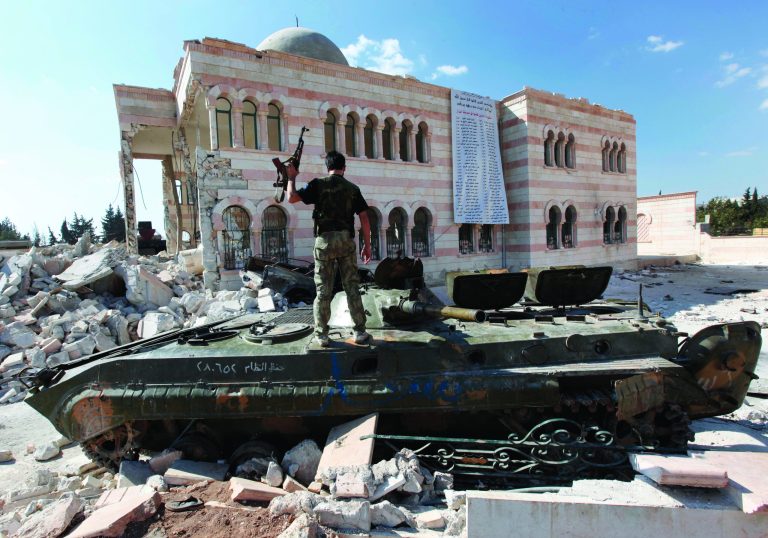 A Free Syrian Army soldier, stands on a damaged Syrian military tank in front of a damaged mosque, which were destroyed during fighting with government forces, in the Syrian town of Azaz, on the outskirts of Aleppo, Sunday, Sept. 23, 2012. Syria's bloody 18-month conflict, which activists say has killed nearly 30,000 people, has so far eluded all attempts at international mediation.(AP Photo/Hussein Malla)