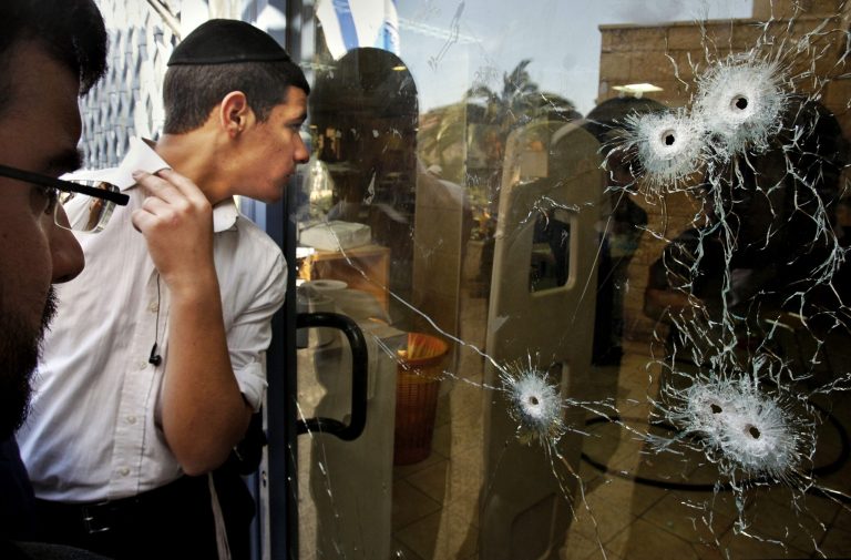   FILE - In this March 7, 2008 file photo an ultra-orthodox Jewish youth peers through a bullet-riddled glass door before the funeral of eight yeshiva students killed in a shooting attack at the Mercaz Harav Yeshiva in Jerusalem. America's top gun lobbyist has his facts wrong when he holds up Israel's stationing of armed guards at all schools as a model of how to avoid another massacre like the Dec. 14, 2012 slaughter of 20 first-graders and six adults at a Connecticut elementary school. What's more, the gun laws in Israel, a country where most people serve in the military, are far more onerous than those in the U.S., containing restrictions that would be anathema to the National Rifle Association and its members. (AP Photo/Kevin Frayer, File)  