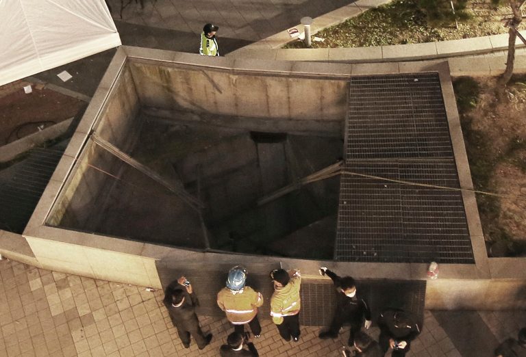 Rescue workers stand around a collapsed ventilation grate at an outdoor theater in Seongnam, South Korea, Friday, Oct. 17, 2014. Fourteen people were feared dead Friday after the ventilation grate collapsed during a concert by popular girlsâ band 4Minute, officials said. (AP Photo/Yonhap, Shin Young-geun) KOREA OUT