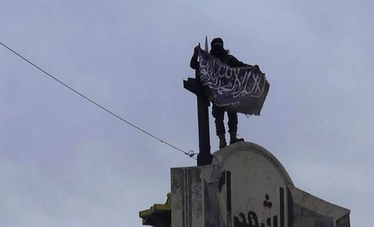 In this image posted on the Twitter page of Syria's al-Qaida-linked Nusra Front on Saturday, March 28, 2015, which is consistent with AP reporting, a fighter from Syria's al-Qaida-linked Nusra Front holds his group flag in Idlib province, north Syria. (AP Photo/Nusra Front on Twitter)