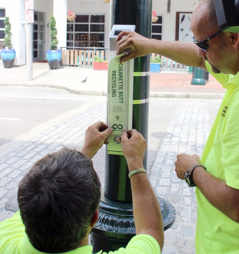Dale Alvin, right, and Jerry Howell apply a label, Monday, July 21, 2014,  to the first of about 50 cigarette butt recycling receptacles they will install in parts of New Orleans with heavy pedestrian traffic. TerraCycle Inc. says the Downtown Development District project is the first large-scale U.S. entry in a cigarette recycling project that started in Canada. (AP Photo/Janet McConnaughey)