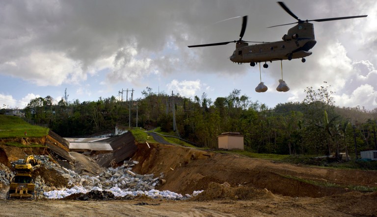 A U.S. Army helicopter transports material to repair the Guajataca Dam, damaged during Hurricane Maria, in Quebradillas, Puerto Rico, Tuesday, Oct. 17, 2017. The dam was built around 1928, and holds back a man-made lake. Some Puerto Rico officials have refused to cooperate with the military and the Federal Emergency Management Agency, according to an Army Corps of Engineers official. (AP Photo/Ramon Espinosa)