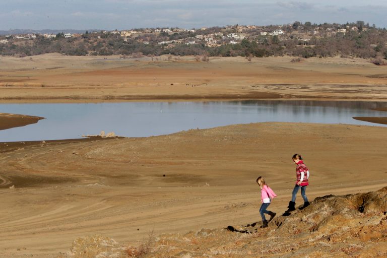 With the edge of California's Folsom Lake more than 100 yards away, girls walk on rocks that are usually at the water's edge, on Jan. 9. (AP Photo/Rich Pedroncelli)