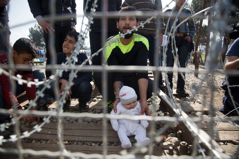 A migrant father with his child awaits on the Greek side of the border to enter Macedonia near the southern Macedonian town of Gevgelija on March 1. Macedonian is restricting the entry of refugees to match the number of those leaving the country, allowing in only refugees from Syria and Iraq, in response to bottlenecks further up along the Balkans migrant route. (AP Photo/Visar Kryeziu)
