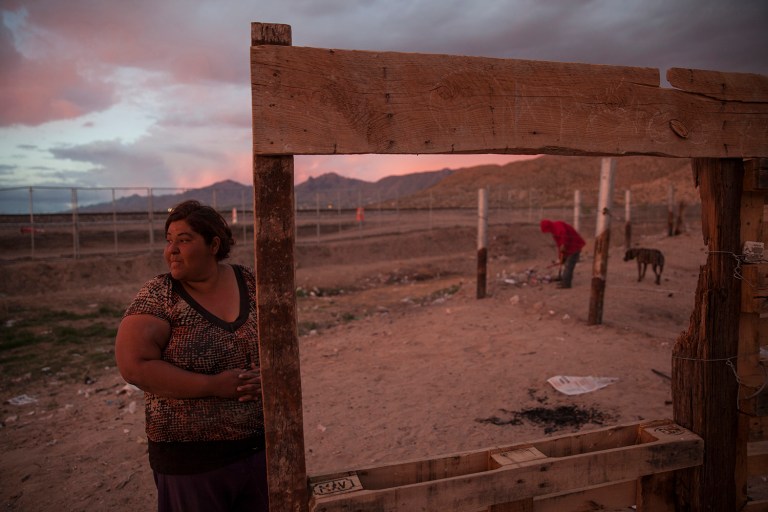 A woman stands outside her home located next to the border fence between the U.S. and Mexico, the gray, metal gate behind her, in the Anapra neighborhood of Ciudad Juarez, Mexico, Wednesday, March 29, 2017, across the border from Sunland Park, New Mexico. This week, Mexican residents like her are losing their view toward the U.S. as each hour a crew welds into place two more segments of steel border fence. (AP Photo/Rodrigo Abd)