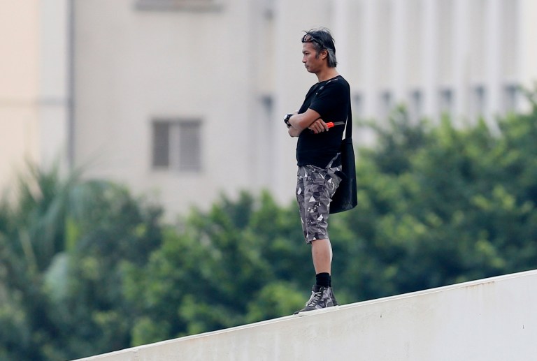 In this Oct. 5, 2014 photo, a man who is identified by local media as Leung Siu Hung, a stuntman, holding a cutter, threatens to jump off the bridge to against the Occupy Central movement outside the government headquarters in Hong Kong's Admiralty. In the Hong Kong protests, not all is as it seems. In the chaos of mass street protests, murky characters come into play.  (AP Photo/Kin Cheung)