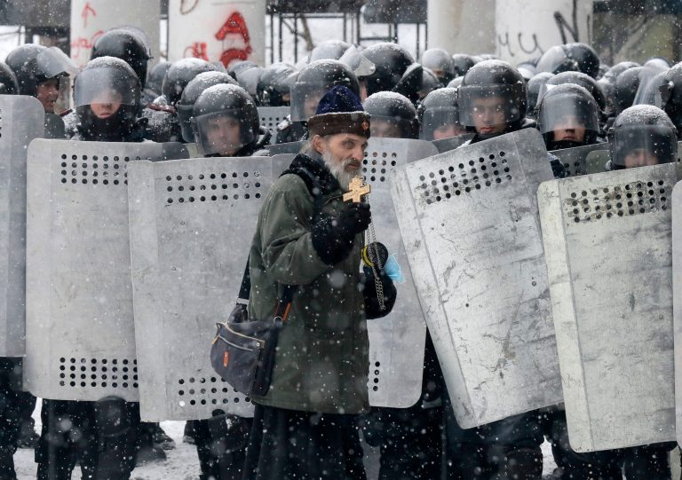 An Orthodox priest prays in front of police officers as they block a street after clashes in central Kiev, Ukraine, on Wednesday. (AP Photo/Efrem Lukatsky)