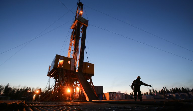 A worker passes an oil drilling rig in an oilfield in Russia.