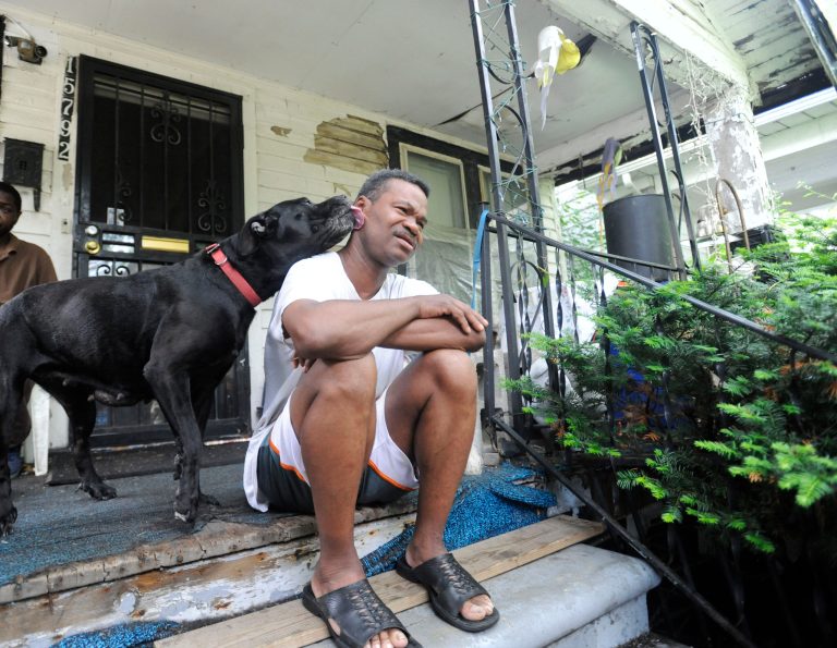 Joseph Garrett and his dogs Sheba and Shack sit on the porch of the house his family lost to foreclosure in Detroit, Monday July 14, 2014. The Detroit Land Bank now owns his house, but Garrett is hopeful he can stay there. The Detroit Land Bank Authority hopes to come up with a plan later this year on how to deal with homes it is trying to sell that are occupied, officials said. (AP Photo/The Detroit News, David Coates)