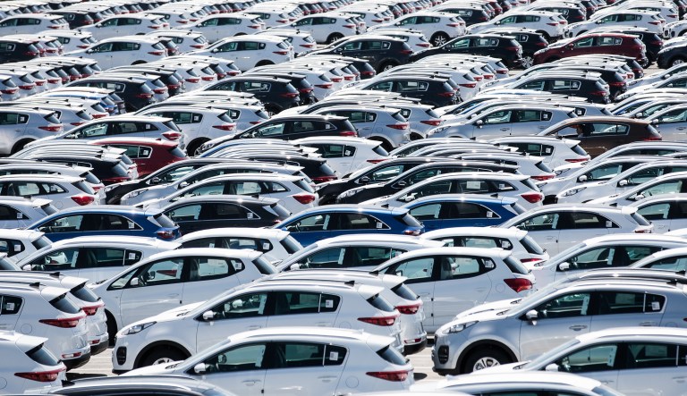 Completed automobiles stand parked in storage outside.