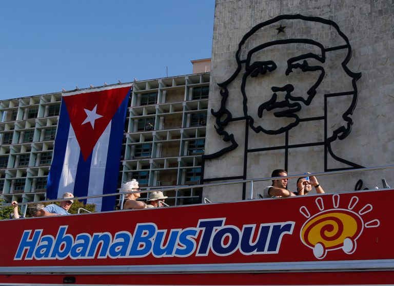 In this March 13, 2015 photo, tourists ride a double-decker bus backdropped by an iron sculpture of Cuban revolutionary hero Ernesto 'Che' Guevara on the facade of the Ministry of Interior in Revolution Square, in Havana, Cuba. Bookings to Cuba jumped 57 percent for one New York tour operator in the weeks after Washington said it would renew ties with Havana. In February, they were up 187 percent; and so far this month, nearly 250 percent. (AP Photo/Desmond Boylan)