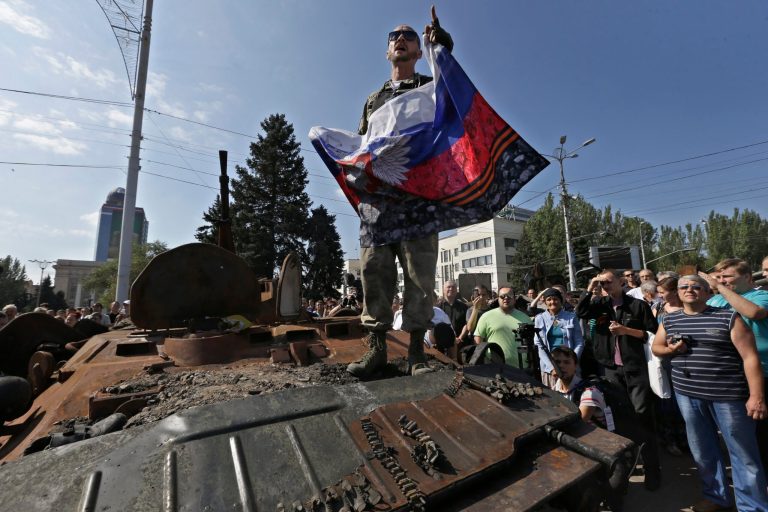 A pro-Russian rebel delivers stands atop a damaged armored personnel carrier of the Ukrainian army on central square in Donetsk, eastern Ukraine, Sunday, Aug. 24, 2014. (AP Photo/Sergei Grits)