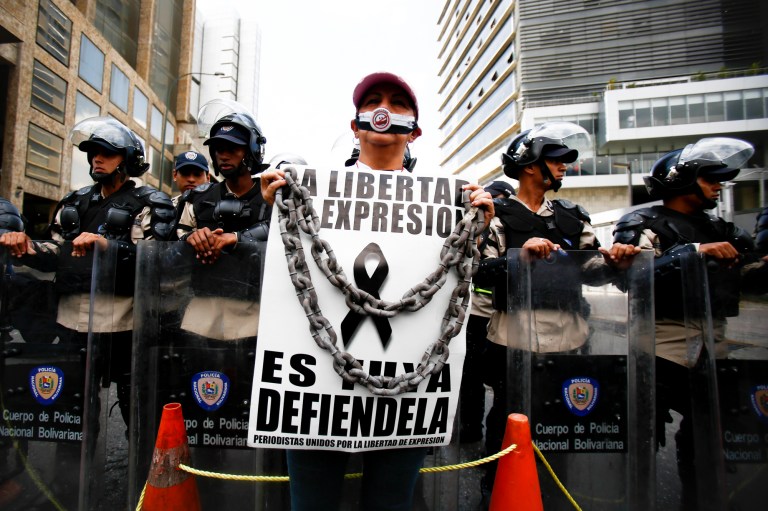 A woman with her mouth covered stands before a line of National Bolivarian Police preventing protesters from reaching the national intelligence agency in Caracas, Venezuela, Tuesday, Feb. 11, 2014. Her sign reads in Spanish 